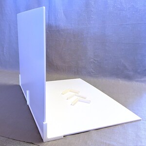 May include: White backdrop for product photography with a white background and a white back panel. The backdrop is made of foam board and has four white plastic corner brackets.