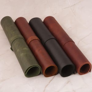Peut inclure: Quatre tapis de bureau enroulés en cuir dans les tons vert, marron, noir et brun rougeâtre. Le tapis vert est fixé avec une sangle en cuir. Les tapis sont disposés en diagonale, mettant en valeur leurs textures et couleurs. Le cuir semble être de haute qualité.