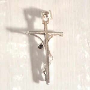 May include: A silver crucifix pendant, featuring a detailed representation of Jesus on the cross. The pendant has a loop for a chain and intricate detailing on the figure and cross.