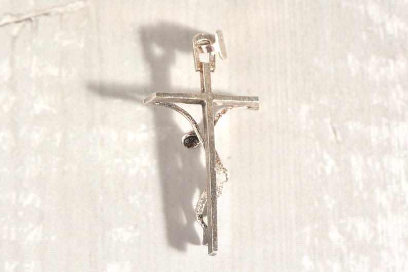 May include: A silver crucifix pendant, featuring a detailed representation of Jesus on the cross. The pendant has a loop for a chain and intricate detailing on the figure and cross.