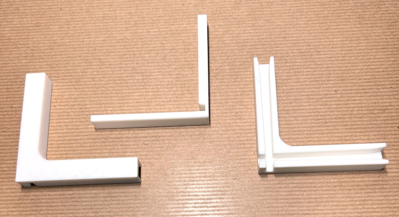 May include: Three white plastic corner brackets, two with a simple L-shape and one with a more complex design featuring a double-layered corner.