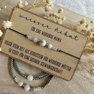Könnte beinhalten: Ein weißes Achat-Armband mit einer Karte, auf der "weisser Achat" und "FÜR EINE WERDENDE MAMA" und "DIESER STEIN GILT ALS SCHUZSTEIN FÜR WERDENDE MÜTTER. ER STEHT FÜR EINE GESUNDE SCHWANGERSCHAFT." steht.