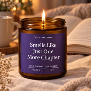 May include: A lit soy candle in an amber glass jar with a purple label. The label reads CANDLESARTSHOP, Smells Like Just One More Chapter, 100% NATURAL SOY CANDLE, 8 oz/250 g, and 40 h. The candle features a single burning wick with a bright flame.