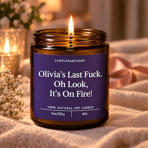 Peut inclure: Une bougie allumée dans un pot en verre ambré avec une étiquette violette. L'étiquette indique : CANDLESARTSHOP, Olivia’s Last Fuck. Oh Look, It’s On Fire!, 100% NATURAL SOY CANDLE, 8 oz/250 g, 40 h. La bougie a une mèche allumée.