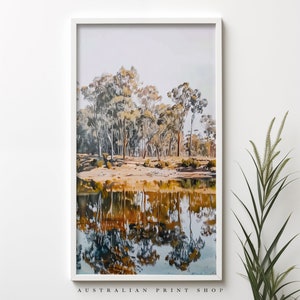 May include: A framed print of a landscape scene with a reflection of trees in a still body of water. The trees are a mix of green and brown, and the water is a light blue color. The print is framed in a white frame.