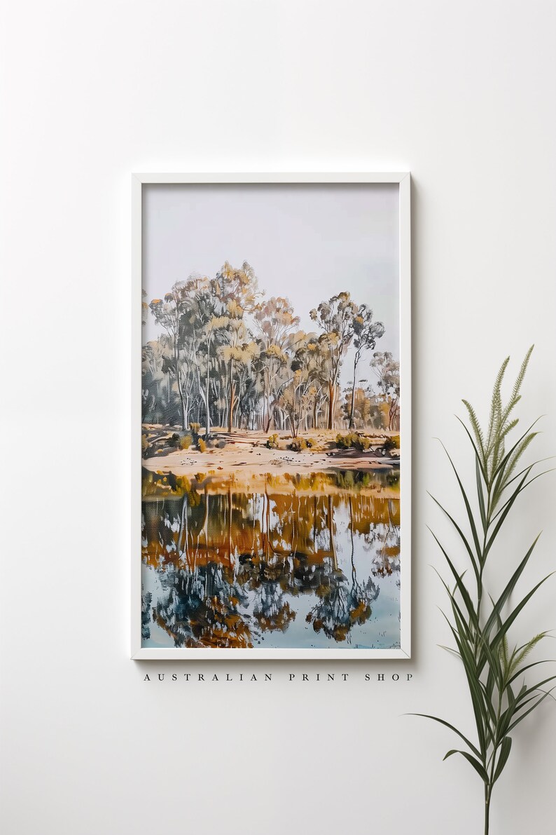 May include: A framed print of a landscape scene with a reflection of trees in a still body of water. The trees are a mix of green and brown, and the water is a light blue color. The print is framed in a white frame.