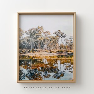 May include: A framed print of a landscape painting featuring a reflection of trees in a still body of water. The trees are a mix of green and brown, and the water is a deep blue with hints of orange and yellow. The frame is a simple gold color.