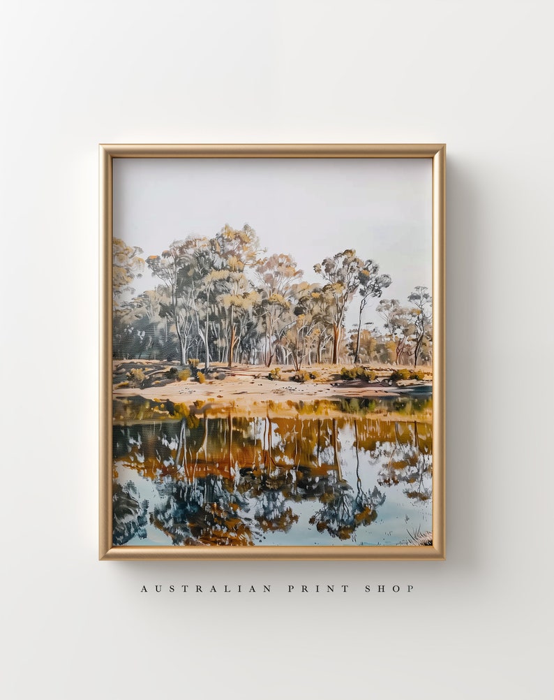May include: A framed print of a landscape painting featuring a reflection of trees in a still body of water. The trees are a mix of green and brown, and the water is a deep blue with hints of orange and yellow. The frame is a simple gold color.