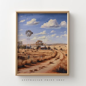 May include: A framed painting of a rural Australian landscape with a windmill, a farmhouse, and a dirt road leading into the distance. The sky is blue with white clouds. The painting is in a gold frame.