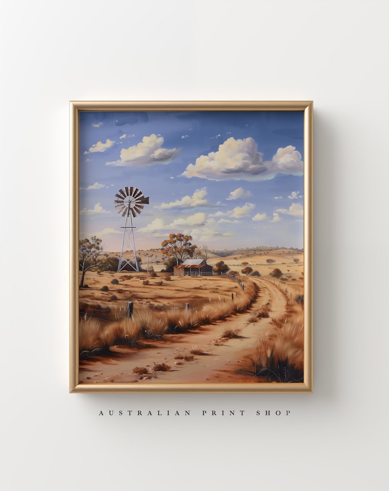 May include: A framed painting of a rural Australian landscape with a windmill, a farmhouse, and a dirt road leading into the distance. The sky is blue with white clouds. The painting is in a gold frame.
