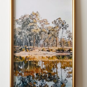 May include: A framed painting of a landscape with trees reflected in a still body of water. The trees are a mix of green and brown, and the water is a deep blue with hints of gold. The frame is gold.