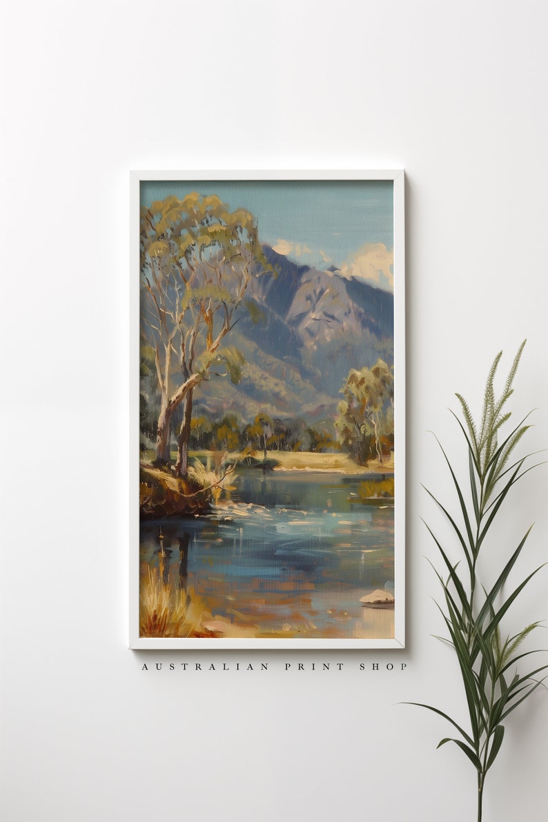 May include: A framed painting of a landscape scene with a river, trees, and mountains in the background. The painting is in a white frame and has a blue and green color scheme. The text "AUSTRALIAN PRINT SHOP" is at the bottom of the frame.