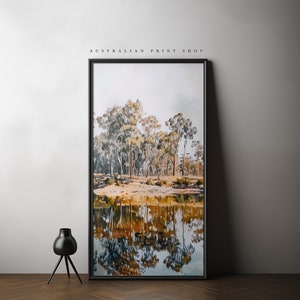 May include: A framed watercolor painting of a forest scene with trees reflected in a still body of water. The painting is in a black frame and is hanging on a white wall.