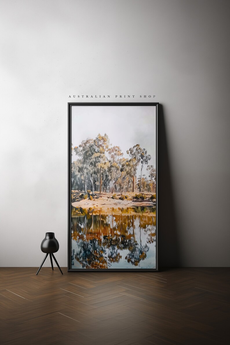 May include: A framed watercolor painting of a forest scene with trees reflected in a still body of water. The painting is in a black frame and is hanging on a white wall.