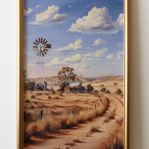 May include: A framed painting of a rural Australian landscape with a windmill, a small farmhouse, and a dirt road leading into the distance. The sky is blue with white clouds. The painting is in a gold frame.