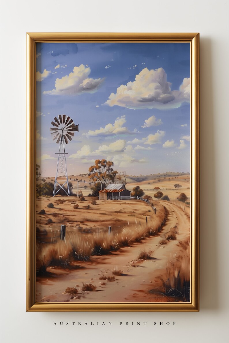 May include: A framed painting of a rural Australian landscape with a windmill, a small farmhouse, and a dirt road leading into the distance. The sky is blue with white clouds. The painting is in a gold frame.