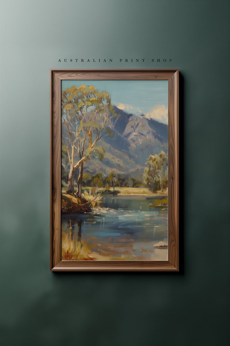 May include: A framed painting of a landscape scene with a river, trees, and mountains in the background. The painting is in a wooden frame and has a rustic feel.