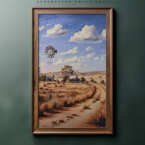 May include: A framed painting of a rural Australian landscape with a windmill, a farmhouse, and a dirt road winding through the dry, brown fields under a blue sky with white clouds.