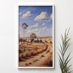 May include: A painting of a rural Australian landscape with a windmill, a small wooden building, and a dirt road leading into the distance. The sky is blue with white clouds. The scene is painted in a realistic style.