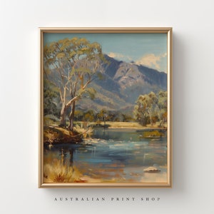 May include: A framed painting of a landscape scene with a river, trees, and mountains in the background. The sky is blue and the water is a light blue. The trees are green and brown. The mountains are gray and brown.