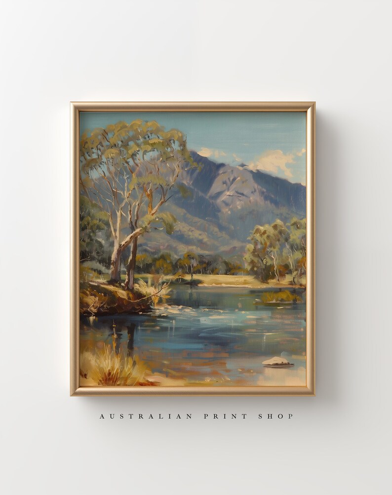 May include: A framed painting of a landscape scene with a river, trees, and mountains in the background. The sky is blue and the water is a light blue. The trees are green and brown. The mountains are gray and brown.