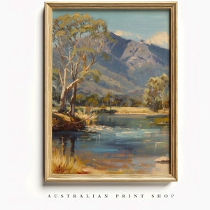 May include: A framed painting of a landscape scene with a river, trees, and mountains in the background. The sky is blue and the water is a light blue. The trees are green and the mountains are gray.