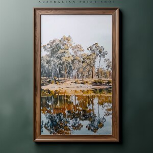May include: A framed print of a painting depicting a reflection of trees in a still body of water. The trees are a mix of green and brown, and the water is a light blue with hints of yellow and orange.