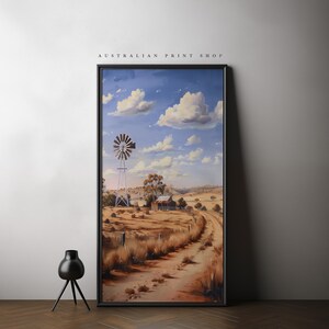 May include: A framed painting of a rural Australian landscape with a windmill, a farmhouse, and a dirt road leading into the distance. The sky is blue with white clouds.