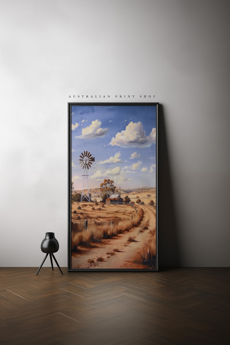 May include: A framed painting of a rural Australian landscape with a windmill, a farmhouse, and a dirt road leading into the distance. The sky is blue with white clouds.