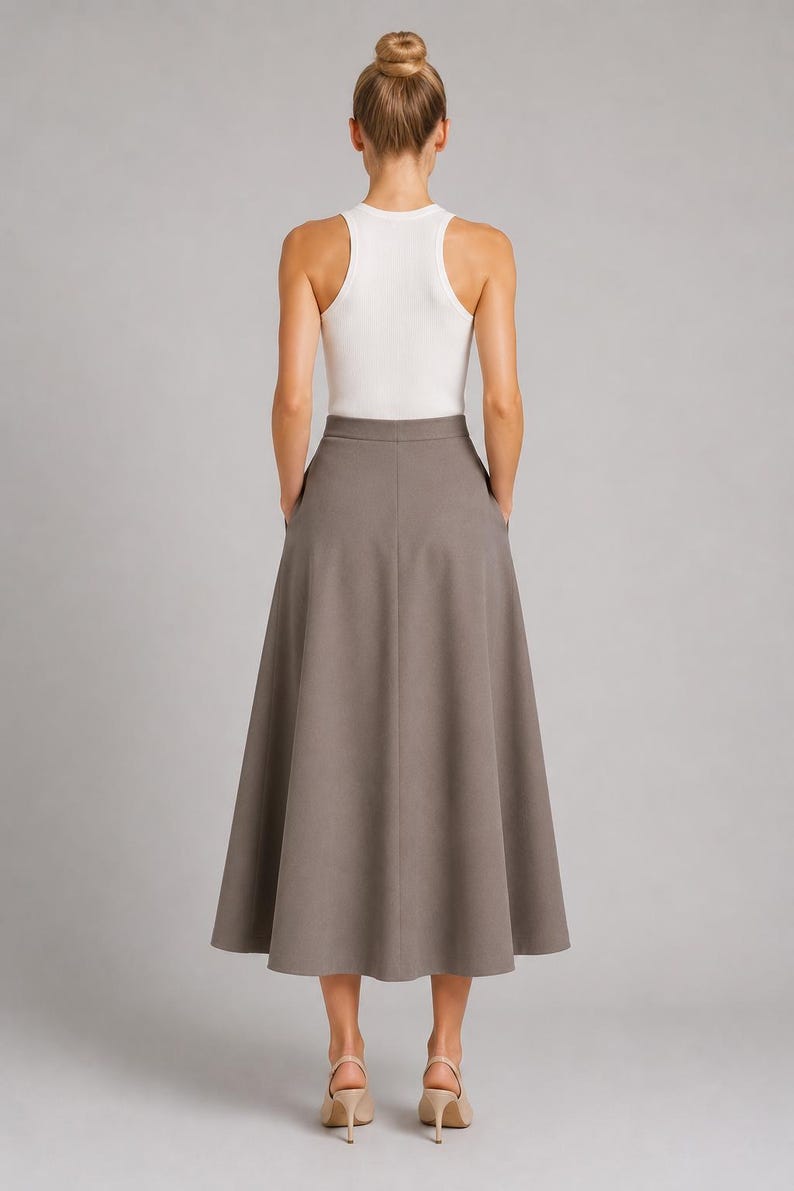 May include: A white sleeveless racerback tank top paired with a solid taupe midi skirt. The skirt features a high-waisted design, a flared A-line silhouette, and side pockets. The ensemble is completed with beige heeled sandals.