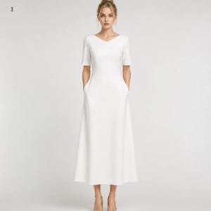 May include: A solid white midi-length dress featuring a V-neckline, short sleeves, and a fitted bodice that transitions into a flared A-line skirt. The garment includes two side pockets integrated into the seams of the skirt, providing a clean look.