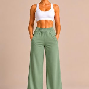 May include: A white racerback sports bra paired with sage green wide-leg sweatpants featuring an elastic waistband and two side pockets. The sweatpants have a loose, straight-leg fit that extends to the ankles, complemented by white sneakers.
