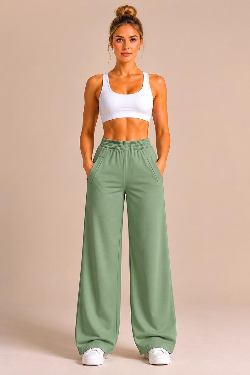 May include: A white racerback sports bra paired with sage green wide-leg sweatpants featuring an elastic waistband and two side pockets. The sweatpants have a loose, straight-leg fit that extends to the ankles, complemented by white sneakers.