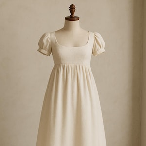 May include: A simple, off-white, sleeveless dress with a gathered skirt and puff sleeves. The dress is made of a lightweight fabric and has a classic, timeless design.