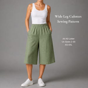 May include: Wide leg culottes sewing pattern in sage green with an elastic waistband and side pockets. The text reads Wide Leg Culottes Sewing Pattern, A4 A0 Letter, US Sizes 2-30, XS-4XL. Paired with a white tank top and white sneakers.