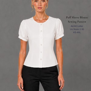May include: A white blouse with short puff sleeves, a round neckline, and a vertical button-down front. The text on the right reads: Puff Sleeve Blouse Sewing Pattern, A4 A0 Letter, Us Sizes 2-30, XS-4XL. The blouse is paired with black trousers.