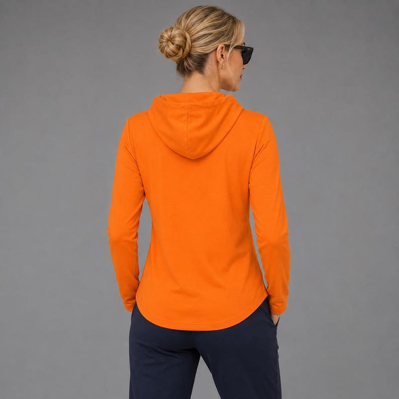 May include: A bright orange long-sleeve hooded pullover shirt with a hood and a curved hemline, paired with dark navy blue pants. The garment features a solid color design with long sleeves and a hood, providing a simple and functional appearance.