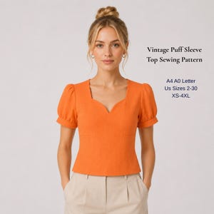 May include: An orange puff sleeve top with a square neckline. The top is part of a sewing pattern, with text indicating sizes from XS to 4XL. The model is wearing the top with beige pants.