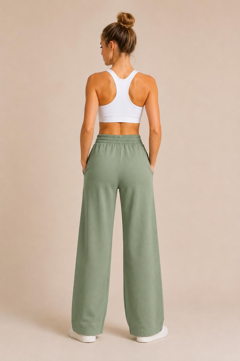 May include: A white racerback sports bra paired with sage green wide-leg sweatpants. The sweatpants feature a high-rise elastic waistband with a drawstring-free design and two side pockets. The fabric has a smooth, solid-colored finish.