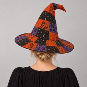 May include: A pointed witch hat featuring a patchwork design of orange, black, and purple fabric panels. The orange sections display a black leaf pattern, while the black panels are decorated with gold crescent moons and small star motifs.