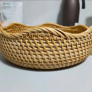 May include: A woven wicker basket with a rounded, wavy rim. The basket is made of natural, light brown material and has a woven pattern.