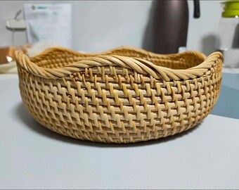 May include: A woven wicker basket with a rounded, wavy rim. The basket is made of natural, light brown material and has a woven pattern.