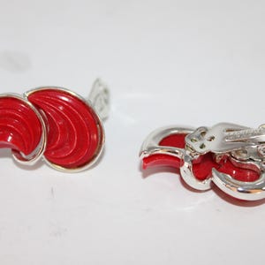 May include: A pair of vintage clip-on earrings. Each earring features a vibrant red, fan-shaped design with a silver-tone metal frame. The earrings have a clip-on closure for non-pierced ears.