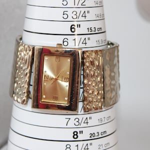 May include: Gold-toned watch with a rectangular face and a textured band. The watch face displays the brand name "No Limit". The watch is shown on a white measuring cone, with the size at 6 inches (15.3 cm).