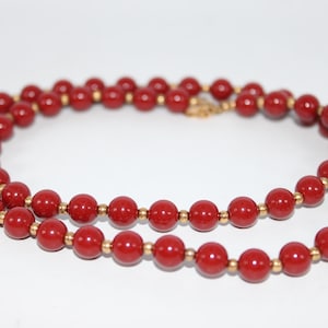 May include: A red beaded necklace with gold-colored accents. The necklace features round, polished red beads strung together with small gold-colored beads. The necklace is displayed against a white background.