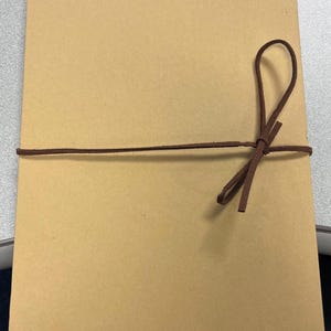 May include: A brown cardboard box with a brown leather cord tied around it in a bow.