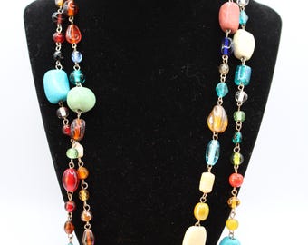 May include: A colorful beaded necklace displayed on a black mannequin. The necklace features a variety of beads in shades of red, orange, yellow, green, blue, and white. The beads are strung together with silver-colored metal.