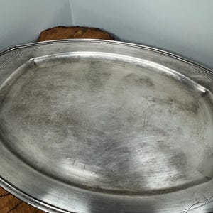 May include: A silver oval serving tray with a decorative border. The tray has a slightly worn, aged look.