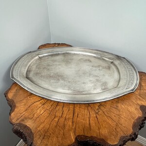 May include: A silver oval serving tray with a decorative border sits on a wooden stump.
