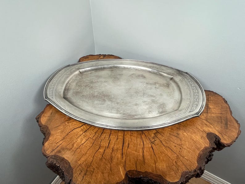 May include: A silver oval serving tray with a decorative border sits on a wooden stump.